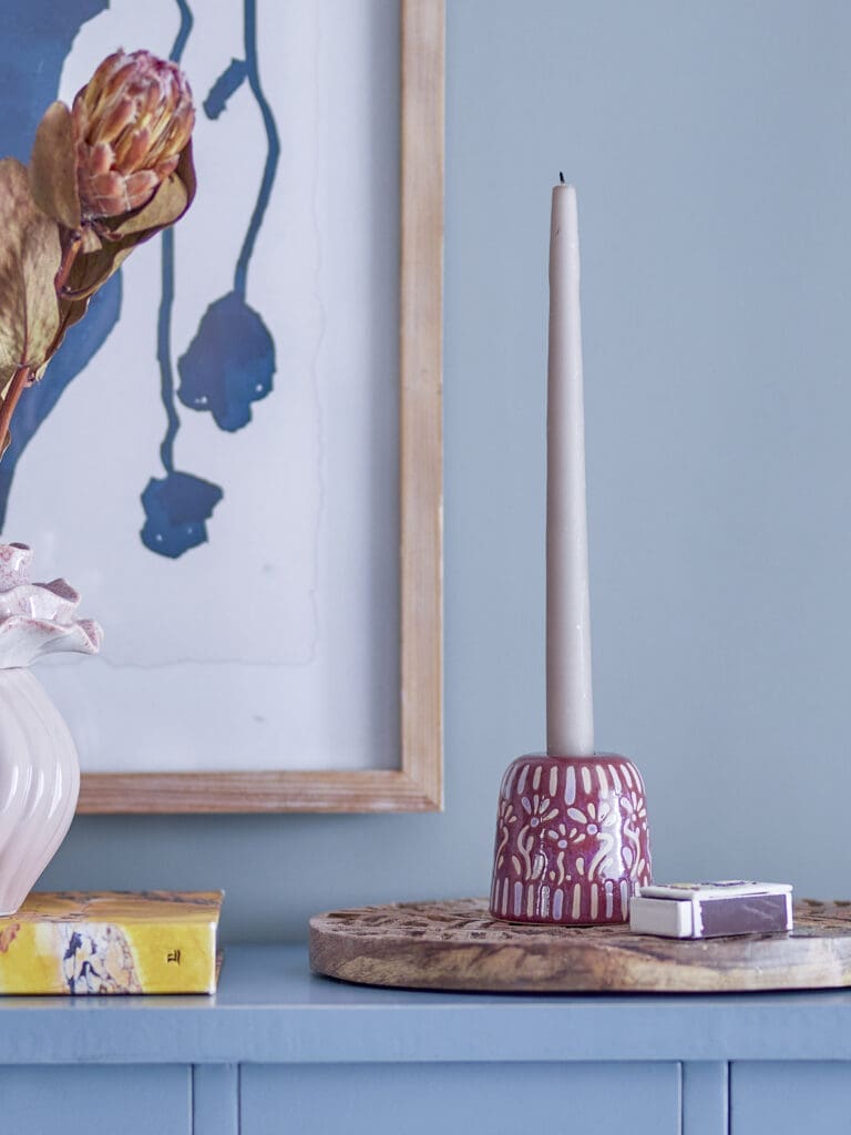 Roze keramieken kandelaar met dinerkaars gestyled op een houten plateau met vaas en kunstwerk.